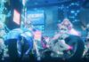 4 of the characters from Chasing Kaleidoriders as they sit on their motorbikes in the middle of a cyberpunk-style city as they look up at something in the game's PV trailer.